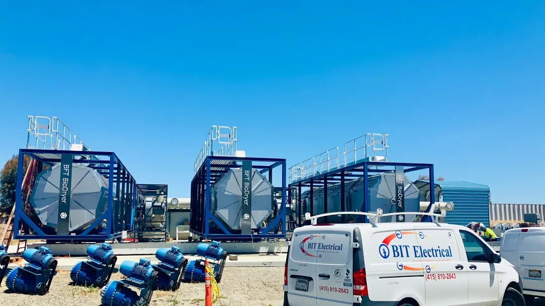 Industrial machinery setup with Bit Electrical Inc. vans and workers at a site under a clear blue sky.