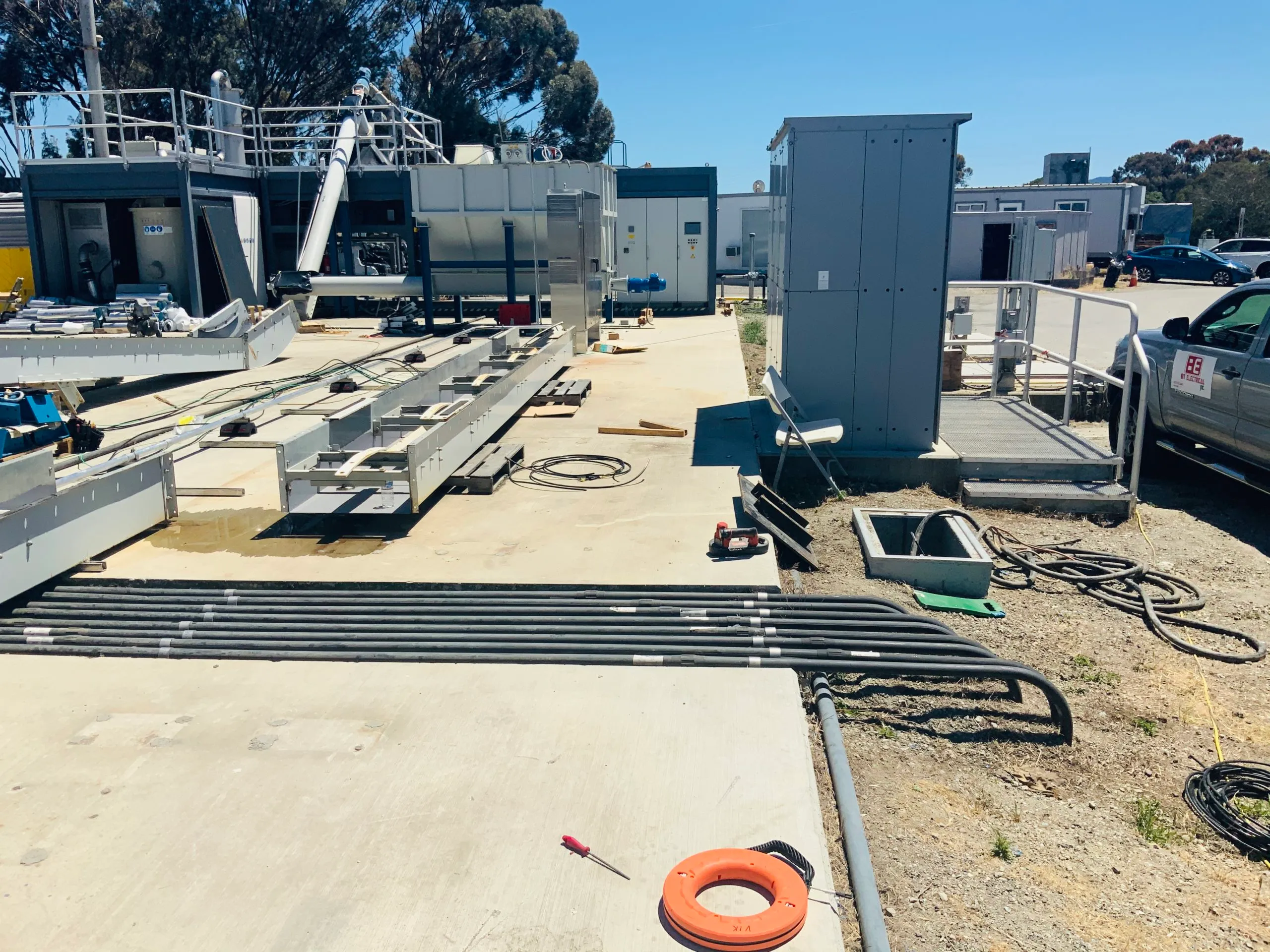  Industrial worksite with arranged cables, electrical panels, and equipment on a concrete surface, set against a clear blue sky.