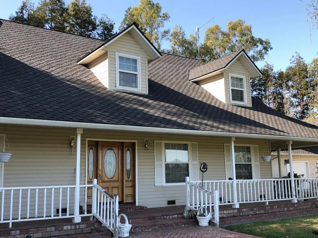 A house with a steep, shingled roof, two dormer windows, and a wooden front door, surrounded by trees. A house with a steep, shingled roof, two dormer windows, and a wooden front door, surrounded by trees.