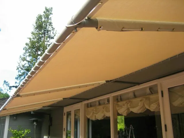  Beige retractable sunshades installed over glass doors, with a tree visible in the background.