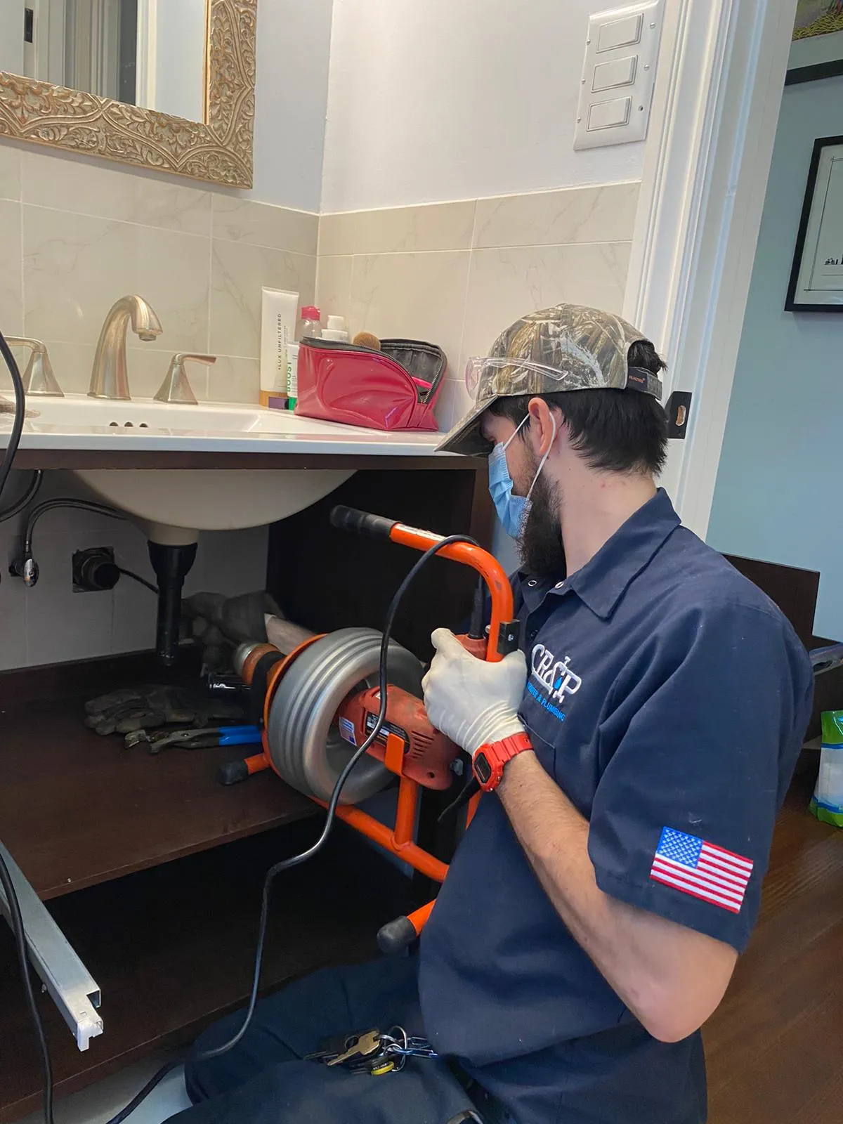 Picture of A technician from Chosen Rooter & Plumbing, Inc. diligently works under a bathroom sink, using a drain cleaning machine to ensure a smooth flow. This attention to detail reflects the company's commitment to quality outcomes, earning them high customer satisfaction ratings. Copyright ©2025 Diamond Certified Resource - Chosen Rooter & Plumbing, Inc.