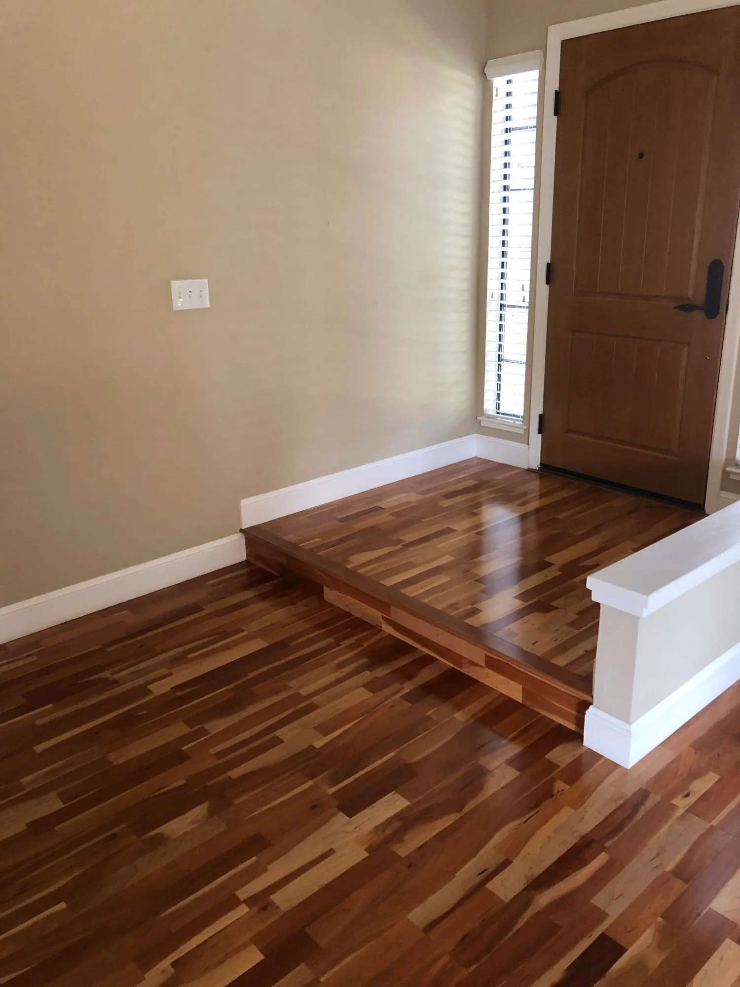 Entrance area with newly installed hardwood floors, a small step, beige walls, and a wooden door with a window beside it.