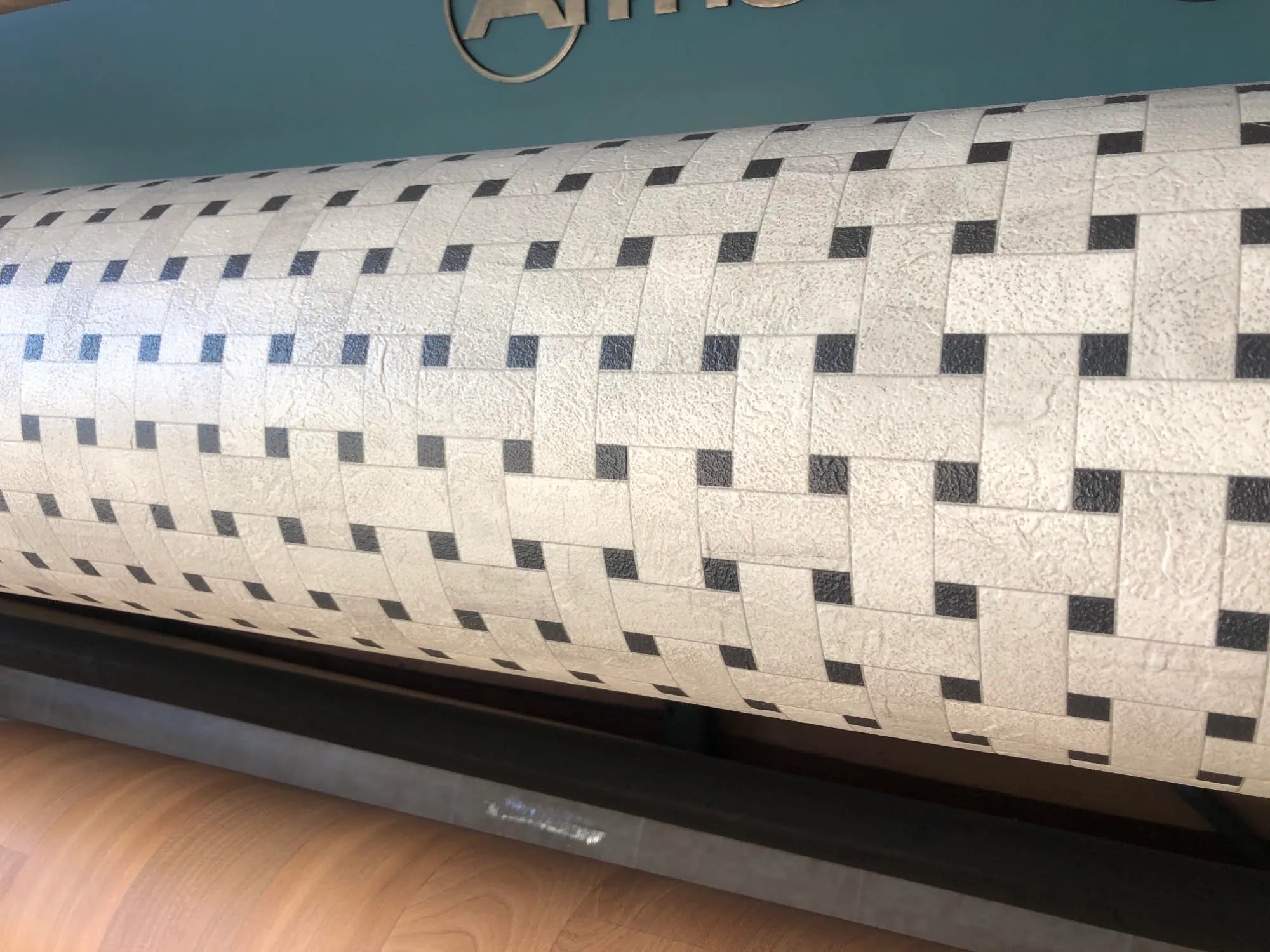 Close-up of a roll of textured carpet with a woven pattern in shades of white and black, displayed on a mechanical loom.