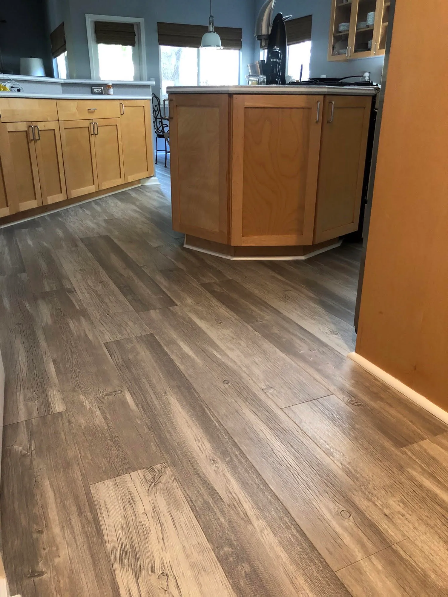 A kitchen with light wood cabinetry and newly installed wood-patterned laminate flooring.
