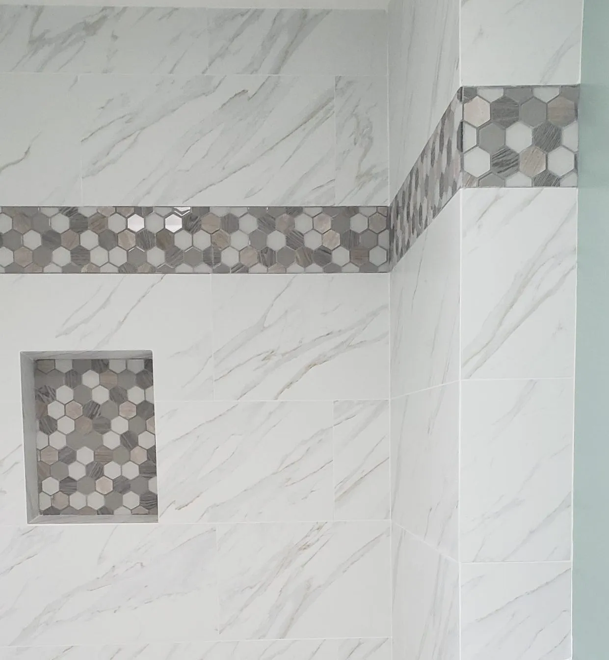 Picture of  A Ramos Construction, Inc. reveals the elegance of a marble-patterned shower with a hexagonal tile accent, showcasing their focus on quality outcomes in every detail. Copyright ©2025 Diamond Certified Resource.

 - A Ramos Construction, Inc.