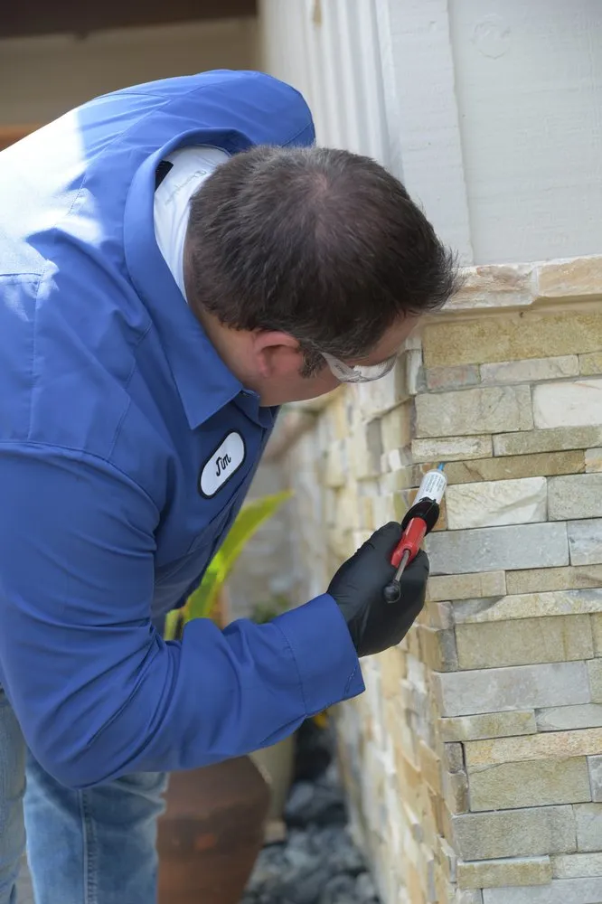 Picture of A Presto Pest Control, Inc. technician, wearing safety glasses and gloves, inspects a stone exterior, demonstrating the company’s commitment to quality outcomes. Recognized for expertise and quality, they ensure homes remain pest-free. Copyright ©2025 Diamond Certified Resource. - Presto Pest Control, Inc.