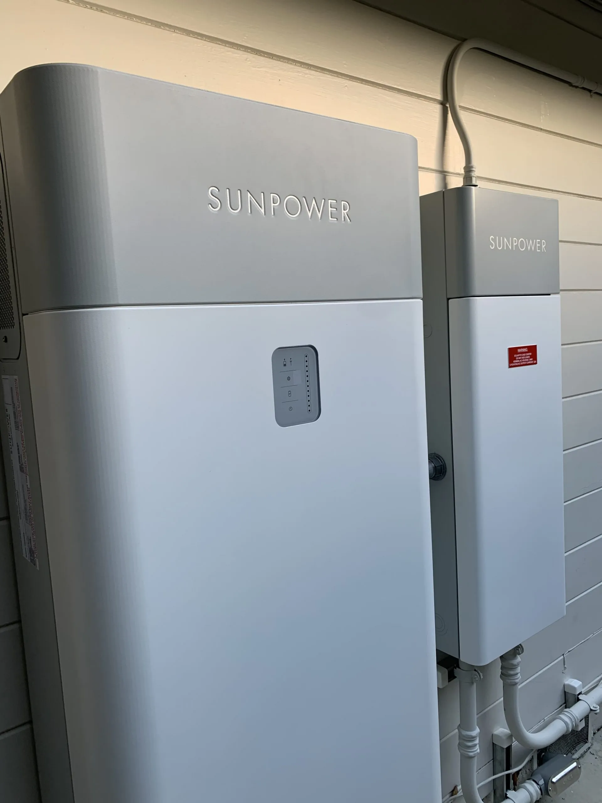  Two SunPower energy storage units mounted on a white wall, with visible cables and connectors.