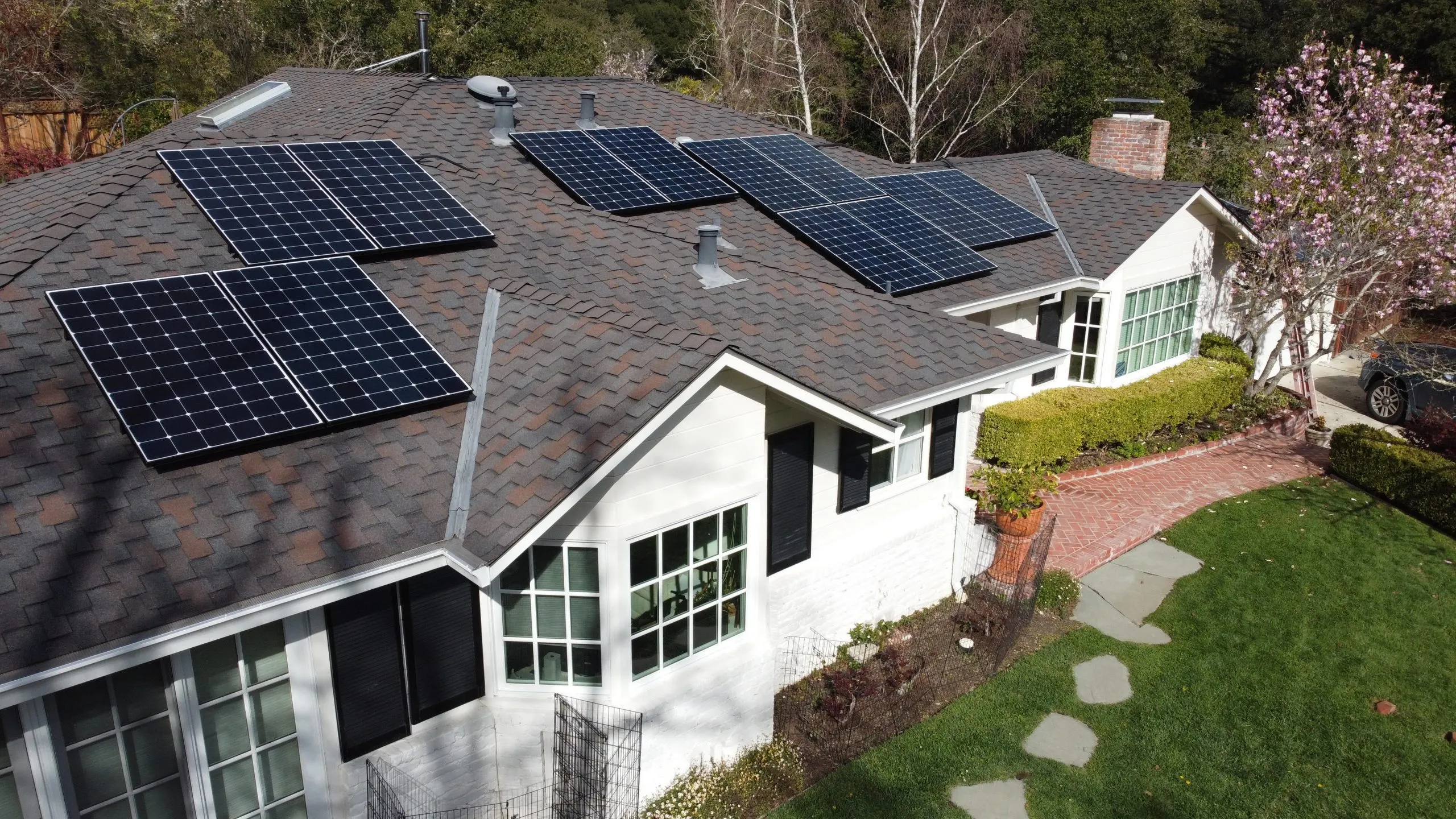 A house with solar panels on its roof, surrounded by green lawn and trees.