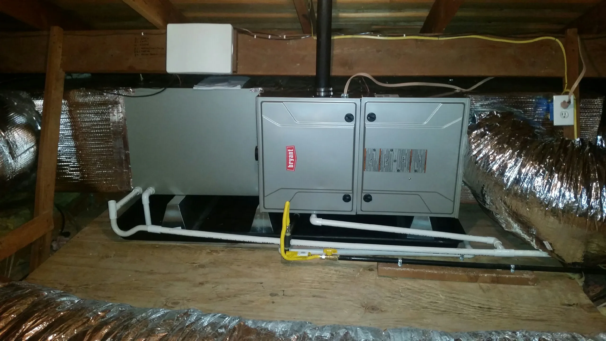 HVAC unit installed in an attic with metallic ducts, wooden beams, and electrical wiring visible. HVAC unit installed in an attic with metallic ducts, wooden beams, and electrical wiring visible.