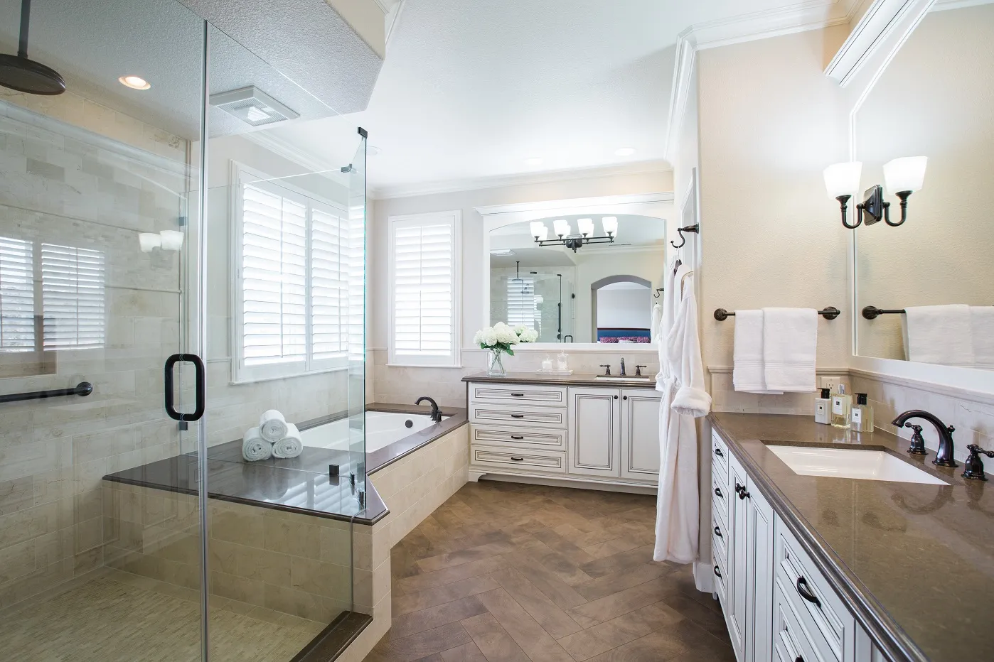 Spacious bathroom with a glass shower, bathtub, dual vanity, and wooden flooring, featuring white cabinets and towels. Spacious bathroom with a glass shower, bathtub, dual vanity, and wooden flooring, featuring white cabinets and towels.