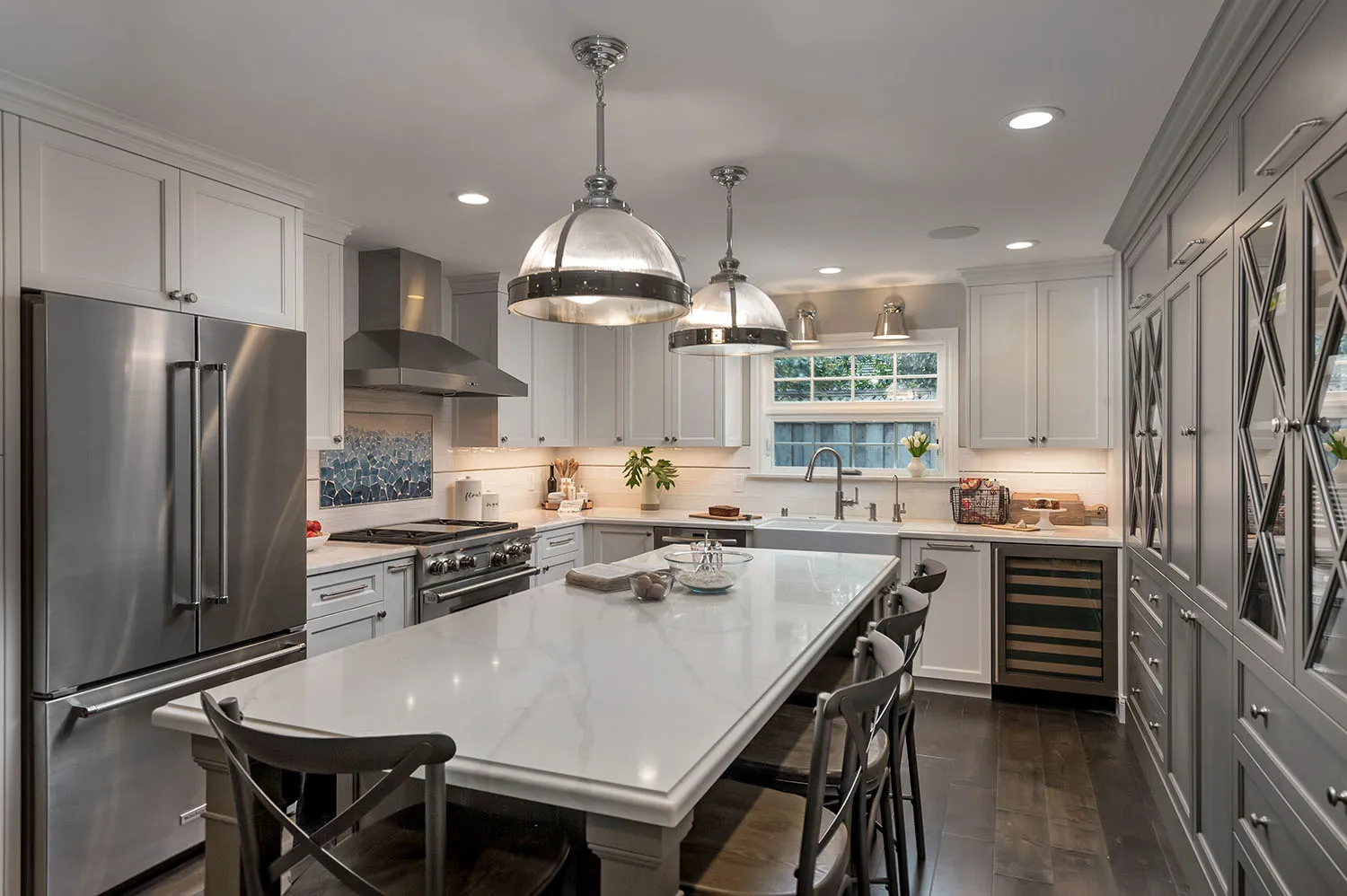 Modern kitchen with a large central island, pendant lights, stainless steel appliances, white cabinets, and a window above the sink.