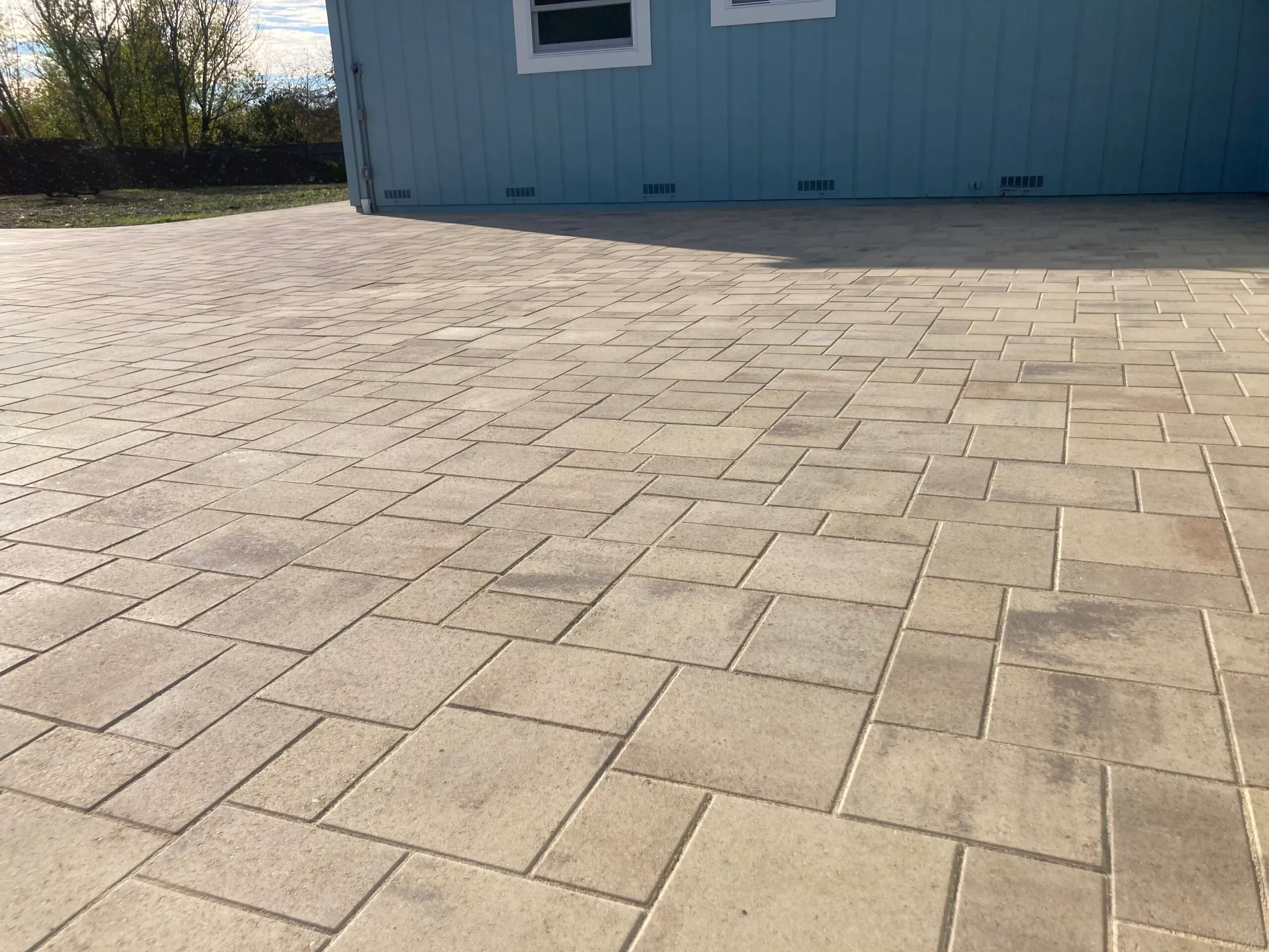 Picture of A meticulously laid stone paver patio extends seamlessly from a modern blue exterior, reflecting The Legacy Paver Group's focus on quality outcomes. Their commitment to precision is evident in every line and joint. Copyright ©2025 Diamond Certified Resource - The Legacy Paver Group