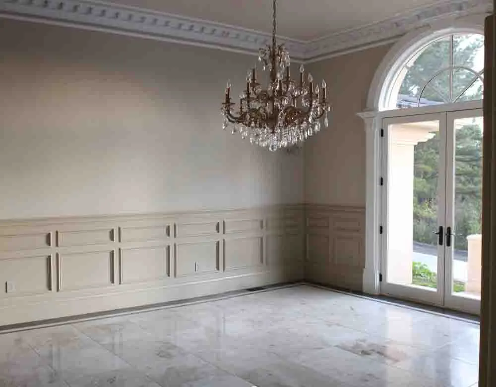 An empty room with detailed wall paneling, a crystal chandelier, marble flooring, and arched double doors leading outside. An empty room with detailed wall paneling, a crystal chandelier, marble flooring, and arched double doors leading outside.