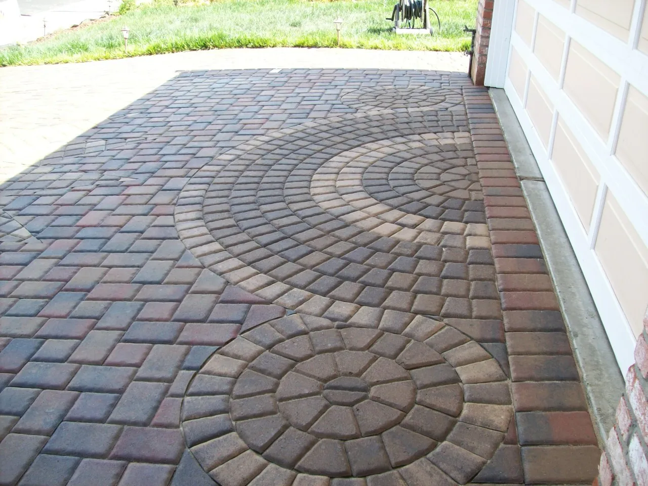 Picture of A meticulously crafted driveway features intricate circular patterns interwoven with precise brickwork, exemplifying Unique Paversâ€™ dedication to quality outcomes. The elegant design seamlessly complements the home's facade, highlighting the companyâ€™s commitment to high customer satisfaction ratings. Copyright ©2025 Diamond Certified Resource

 - Unique Pavers
