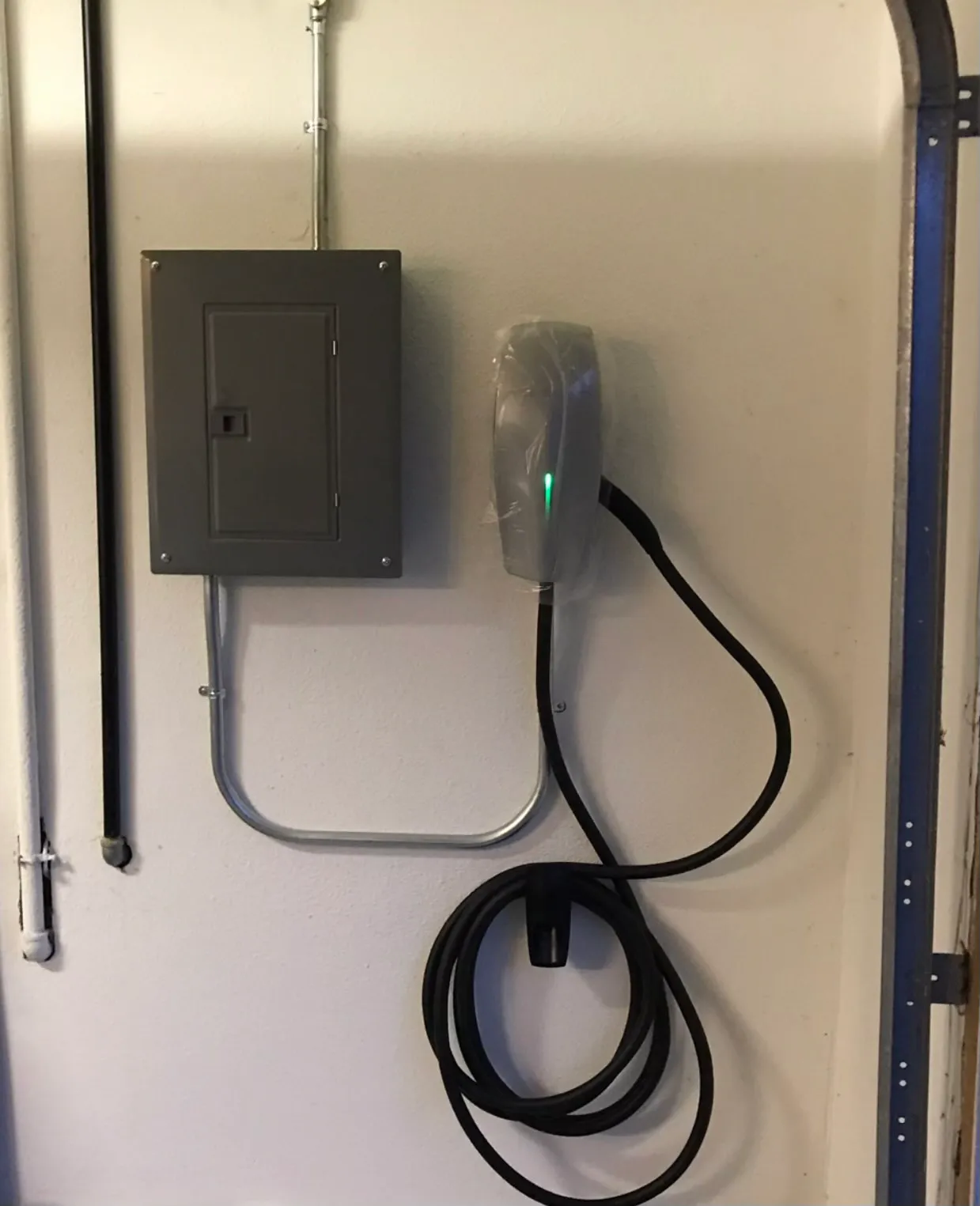 Electric vehicle charger mounted on a wall next to a control panel, with a coiled black cable hanging below.