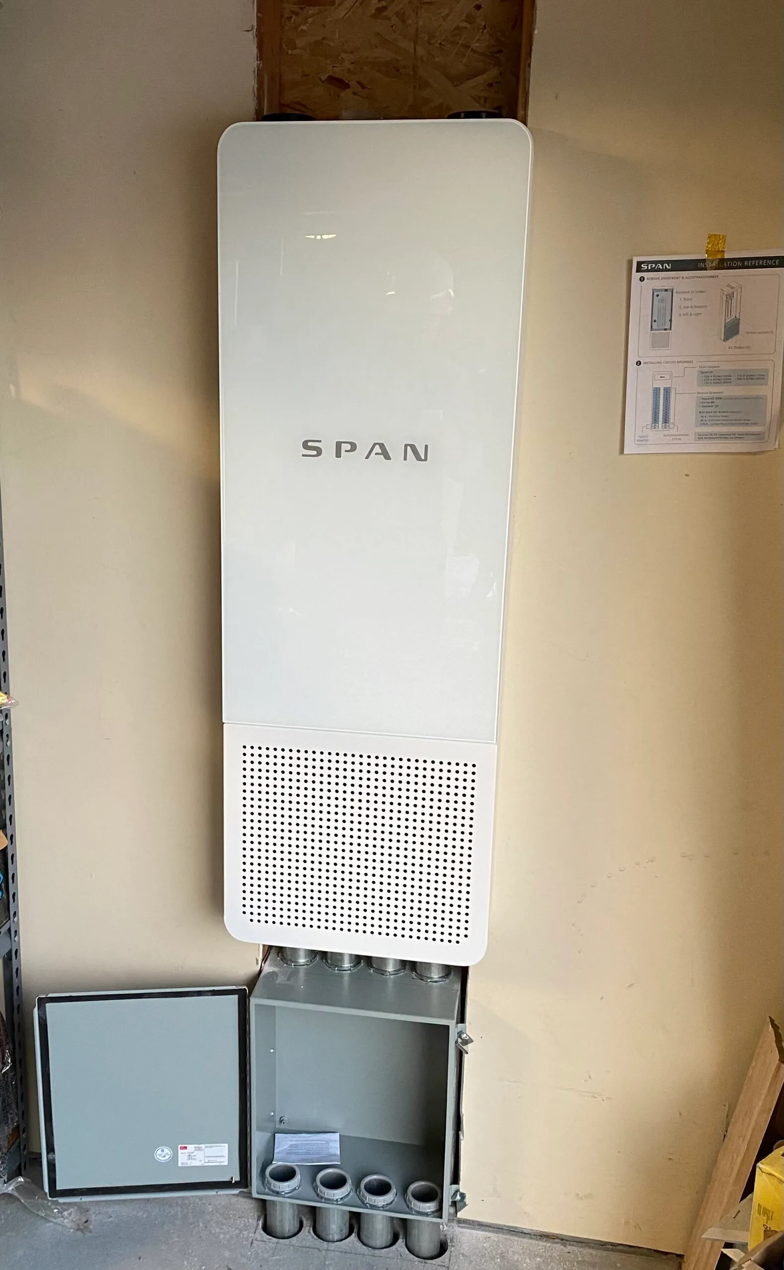  Energy management system with open panel and labeled "SPAN" mounted on a wall. Installation reference guide visible nearby.