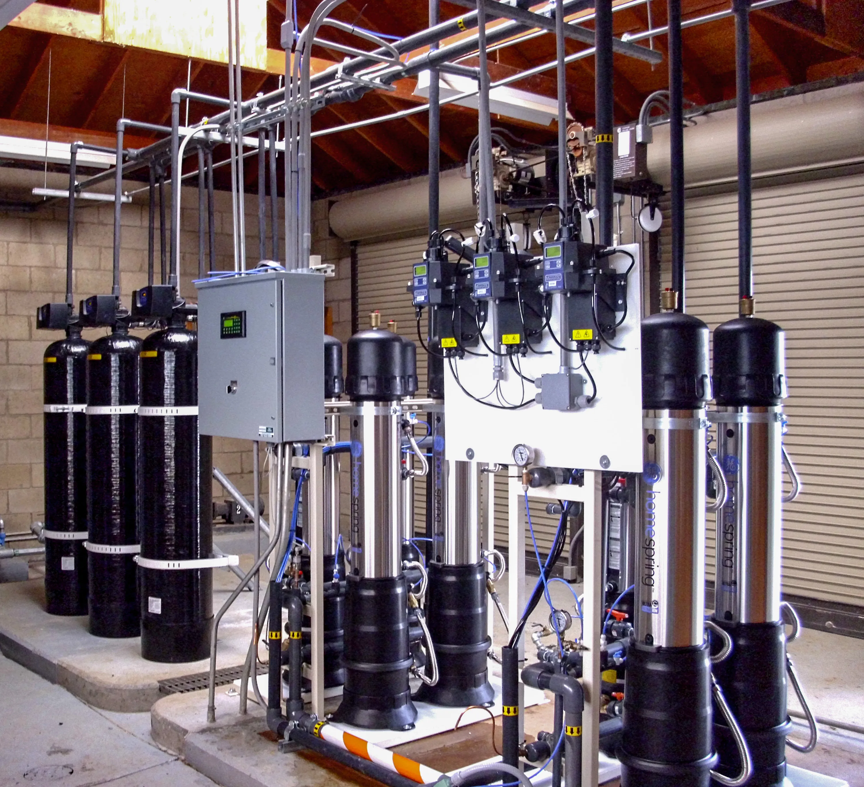  Industrial water treatment facility with multiple pumps, control units, and piping under a wooden ceiling.